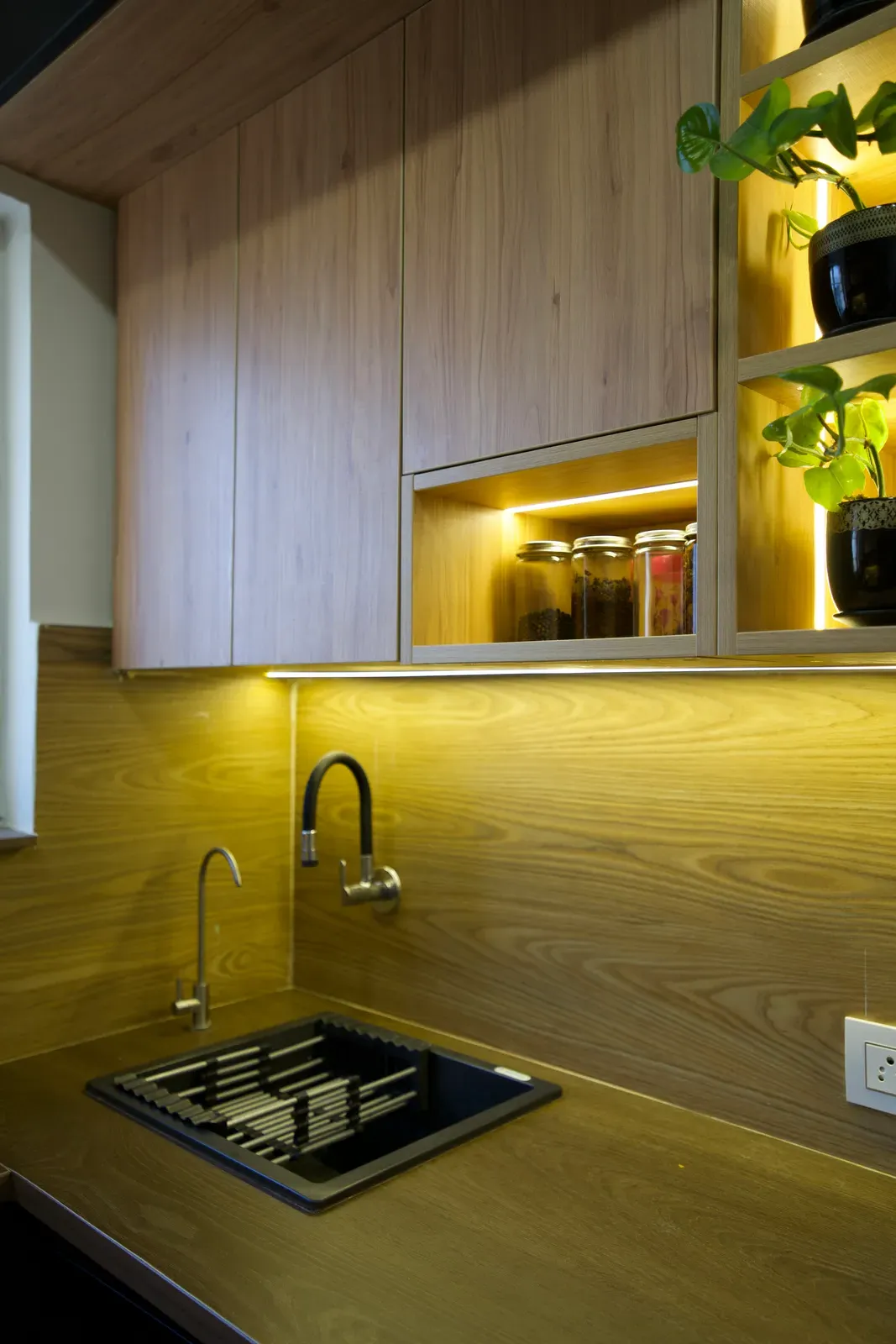 Oak-finish kitchen with lit open shelves above the sink — The Aakar
